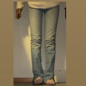 Grå jeans med slits nertill - Blå jeans med hög midja och raka ben. Jeansen har en liten slits nertill vid benslutet. Perfekta till sneakers eller boots för en clean look.