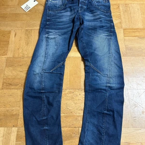 Blå jeansbyxor från Jack & Jones - Säljer ett par blå jeansbyxor från Jack & Jones, modell Stan Twisted JOS 483. Byxorna har normal passform, klassisk femficksdesign och snygga slitningar på benen. Midjan är midwaist och benen har en rak siluett. Storlek W 32 L 32 KOM MED PRISFÖRSLAG