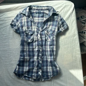 Blårutig kortärmad skjorta från Terranova - Säljer en blårutig skjorta från Terranova i storlek XS. Skjortan har korta ärmar, två bröstfickor med lock och knappar framtill. Perfekt för dig som gillar en klassisk och avslappnad stil.