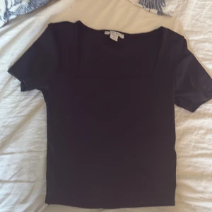 Svart topp med fyrkantig ringning - En stilren svart topp med korta ärmar och fyrkantig ringning. Perfekt att matcha med både jeans och kjol för en enkel men snygg look.