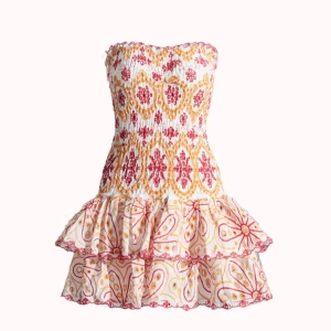 Design by Amor Mönstrad axelbandslös kortklänning - Superfin axelbandslös kortklänning med smockad överdel och volangkjol. Klänningen har ett färgglatt mönster i rött och gult på vit botten och dekorativa volangdetaljer. Perfekt för sommarens alla tillfällen!