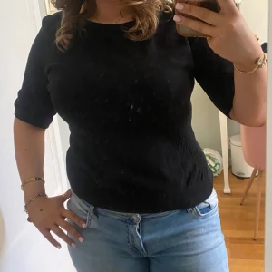 Svart stickad tshirt - Säljer en svart topp från H&M med rund halsringning och korta ärmar. Tröjan har en lätt ribbad struktur vid midjan och är tillverkad i ett mjukt material som passar perfekt till jeans eller kjol. Den har lite mäster vid kragen!