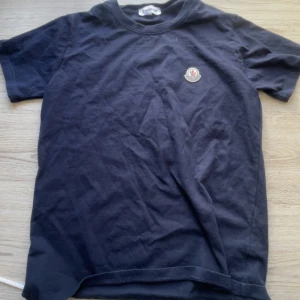 Svart t-shirt från Moncler - Säljer en svart t-shirt från Moncler med klassisk passform och rund hals. T-shirten har Monclers logga broderad på bröstet och är tillverkad i mjuk bomull. Perfekt för en stilren och enkel look.