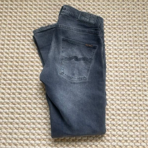 Grå jeans Grim Tim från Nudie Jeans - Säljer ett par gråa Grim Tim jeans från Nudie Jeans. Modellen har klassisk femficksdesign, raka ben och subtila slitningar. 30/30, hör av dig vid minsta fundering!