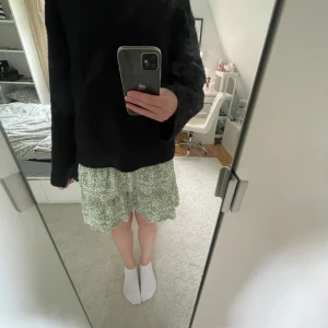 Grön blommig kortkjol - Säljer en söt grön kortkjol med vitt blommönster. Kjolen har en smockad midja och volang nertill som ger en luftig och somrig känsla. Perfekt för dig som gillar en avslappnad och trendig stil.