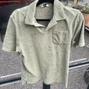 Ljusgrön frottéskjorta från East West - Säljer en ljusgrön skjorta i mjuk frotté från East West. Skjortan har korta ärmar, klassisk krage och en bröstficka. Perfekt för en avslappnad och trendig look.