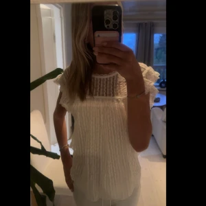 Vit blus med volangdetaljer - Säljer en söt vit blus med volangdetaljer på axlarna och runt ärmslut. Aldrig använd i storlek s