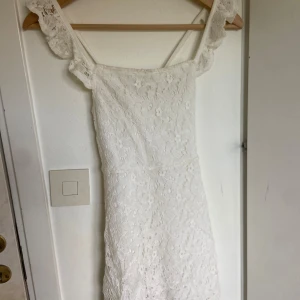 Vit spetsklänning från H&M - Säljer en söt vit barnklänning från H&M med spetsdetaljer i storlek 134/140. Klänningen har en figurnära passform och är fodrad med polyester. Perfekt för somriga tillfällen eller studentfirande. 