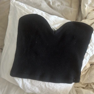 Svart ribbad tubtopp - Säljer en svart ribbad tubtopp med hjärtformad urringning. Toppen är ärmlös och har en tight passform, perfekt att styla till olika outfits.