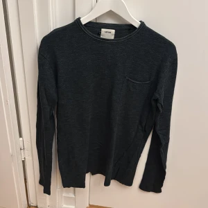 Mörkgrön långärmad tröja från WINWIN - En stilren mörkgrön långärmad tröja från WINWIN. Tröjan har rund halsringning och en liten bröstficka på vänster sida. Perfekt för en enkel och avslappnad look.