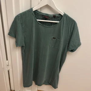 Grön t-shirt från Scotch & Soda - Snygg grön t-shirt från Scotch & Soda med rund halsringning och liten bröstficka. T-shirten har ett diskret mönster på insidan av halsen och är perfekt för en avslappnad stil. Storlek L.