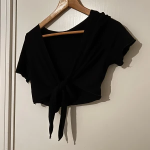 Svart croppad knyt-topp - Säljer en svart croppad topp med kort ärm går att ha som en fin kofta och topp, jätte skönt mjukt material 