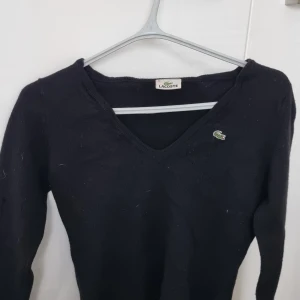 Svart v-ringad tröja från Lacoste - Säljer en klassisk svart v-ringad tröja från Lacoste med den ikoniska krokodilloggan på bröstet. Tröjan har långa ärmar och är perfekt för en stilren och enkel look. V neck tröja Sweatshirt stl xs s