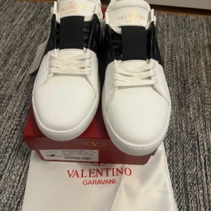 Valentino Garavani sneakers - Säljer ett par vita Valentino Garavani One Stud XL sneakers med svart detalj över mitten. Skorna har rund tå, platt sula och klassisk snörning. Perfekta för dig som gillar stilrena och exklusiva sneakers.