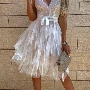 Ljus volangklänning med spets och omlott - Romantisk ljus klänning med v-ringad omlott-topp i spets och flera lager volangig tyllkjol. Midjan markeras med ett satinband och rosett. Perfekt för sommarens speciella tillfällen.