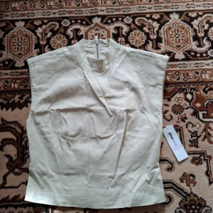 Beige ärmlös topp från Object - Snygg beige ärmlös topp från Object med hög hals och dragkedja i ryggen. Toppen har en stilren och minimalistisk design, perfekt att matcha med olika outfits. Materialet känns mjukt och lätt.