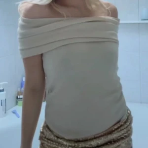 Beige offshoulder topp - Säljer en snygg beige offshoulder topp med draperad kant upptill. Toppen har en stilren och elegant look, perfekt att styla med både kjol och byxor. Materialet känns mjukt och följsamt.