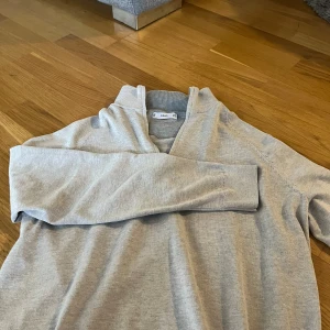 Ljusgrå tröja med dragkedja från Mang - Säljer en stilren ljusgrå tröja från Mango med halv dragkedja i halsen. Tröjan har lång ärm och ribbade detaljer vid krage och ärmslut. Perfekt för lager-på-lager och enkel att matcha med olika outfits.