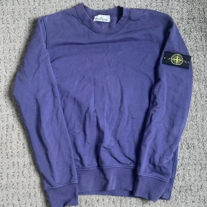 Lila sweatshirt från Stone Island - Säljer en lila sweatshirt från Stone Island med klassisk logotyp-patch på vänster ärm. Tröjan har rund halsringning och långa ärmar med ribbade muddar. Perfekt för en avslappnad och stilren look. Vid mer frågor eller funderingar det är bara att skriva. OBS SKICKAS EJ! Bara avhämtning i Mölndal/Kållered