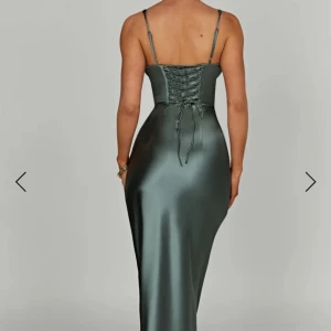 Grön  långklänning i satin från Babyboo - Supersnygg grön långklänning i satin från Babyboo med smala axelband, djup v-ringning och korsettliknande liv. Klänningen har snörning i ryggen och markerad midja för en riktigt elegant siluett.