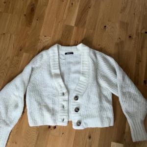 Vit stickad kofta från Gina Tricot - Mysig vit stickad kofta från Gina Tricot med stora knappar framtill. Koftan är croppad och har långa ärmar samt bred ribbad krage. Storlek XS