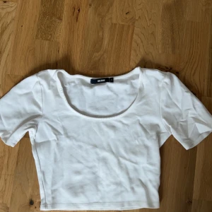 Vit croppad topp från Bik Bok - Säljer en vit croppad topp från Bik Bok med korta ärmar och rundad urringning. Perfekt att matcha med jeans eller kjol för en enkel och fräsch look.