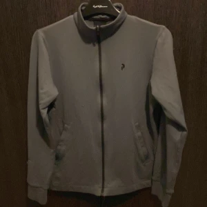 Grå zip golf tröja från Peak Performance - Grå tröja från Peak Performance med hel dragkedja framtill och ståkrage. Diskret logga på bröstet och text med varumärket längs ryggen. Perfekt för en sportig och stilren look. Strl m men sitter som typ s