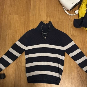 Mörkblå randig tröja med dragkedja från Zara - Mörkblå ribbstickad tröja från Zara med vita horisontella ränder. Tröjan har lång ärm och halv dragkedja vid halsen som ger en sportig look. Perfekt för dig som gillar klassisk stil med en twist. Tänker 70 kr men pris kan diskuteras.