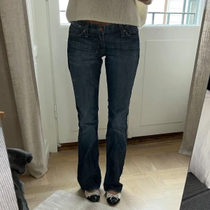 Mörkblå bootcut jeans från Guess - Snygga mörkblå jeans från Guess med bootcut passform och låg midja. Klassisk femficksmodell med diskret logga på bakfickan. Jeansen har en lätt utsvängd benform och stängs med dragkedja och knapp. Sitter snyggt och är i fint skick, storlek 34. Jag är 169 cm lång, och på bilderna är mitt innerbensmått ca 82,5 cm och midjemått (platt mätt på mig) ca 31 cm.