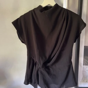 Svart omlottopp med knut  - Snygg svart omlottopp med knut i midjan och korta ärmar. Tidlös design som passar till många olika stilar. Perfekt att matcha med både jeans och kjol.🪸