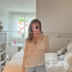 Beige v-ringad blus  - Säljer en tunn och lätt beige v-ringad blus. Blusen har långa ärmar och en avslappnad passform, perfekt att styla med jeans eller kjol. Enkel och stilren design.