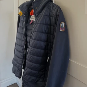 Mörkblå pufferjacka från Parajumpers - Säljer en mörkblå pufferjacka från Parajumpers med quiltad front och ärmar i mjukare material. Jackan har dragkedja, ståkrage med gul detalj och två sidofickor med dragkedja. Märkespatch på ena ärmen.