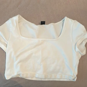 Vit croppad t-shirt med fyrkantig ringning - Säljer en vit croppad t-shirt från Bershka med korta ärmar och fyrkantig ringning. Perfekt till jeans eller kjol för en enkel och fräsch look.