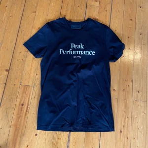 Svart t-shirt från Peak Performance - Snygg svart t-shirt från Peak Performance med vit logga och text på bröstet. Klassisk rund halsringning och korta ärmar. Perfekt för en stilren och sportig look.