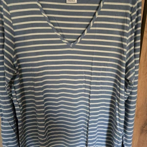 Blå och vit randig långärmad tröja från Voila' - Säljer en blå och vit randig långärmad tröja från Voiid med v-ringad hals. Perfekt för en avslappnad stil och passar året runt. Supermjuk och skön att ha på sig!