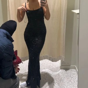 Svart glittrig långklänning med paljetter - Säljer en svart långklänning från BikBok med smala axelband och figurnära passform. Klänningen är täckt av svarta paljetter som ger en glittrig effekt. Använd en gång. 