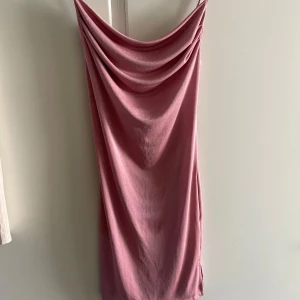 Rosa draperad klänning - Säljer en snygg rosa klänning med draperad urringning och axelbandslös design. Klänningen har en rak passform och är tillverkad i ett mjukt, slätt material som faller fint. Perfekt för sommarens tillfällen!