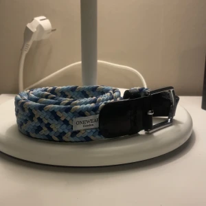 Blått flätat bälte från Onewear Sweden - Snyggt flätat bälte i blått, vitt och beige från Onewear Sweden. Bältet har ett silverfärgat spänne och detaljer i svart skinn. Perfekt accessoar för att lyfta din outfit. Bältet är använt ett fåtal gånger och är som helt nytt. 300 kronor är nypriset och jag säljer för 150. Skriv för fler funderingar eller frågor💯💯💯