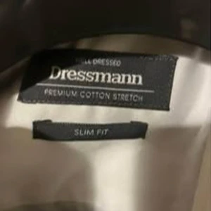 Mörkblå kostym från Dressmann - Säljers en stilren mörkblå kostym från Dressmann i slim fit-modell. Endast använd en gång! Kavajen har klassisk passform med två knappar, fickor med lock och bröstficka för näsduk. Skjortan ingår. Perfekt för bal eller student.                     Mått byxor: 71 cm från grenen till foten (insidan). 95 cm från midjan/bältet till foten (utsidan).  Mått kavaj: Ärm 59 cm, längd från kragen och ned 66 cm, bredd axlar 49 cm, bredd midja 40 cm. 