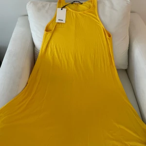 Gul långklänning från BikBok - Säljer en solgul långklänning från BikBok i mjuk bomull. Klänningen är ärmlös med rund halsringning och har en flowy passform som ger en avslappnad look. Perfekt för varma dagar och somriga tillfällen.