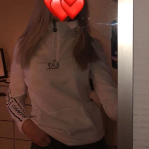 Vit tröja från Emporio Armani EA7 - Säljer en vit långärmad tröja från Emporio Armani EA7 med dragkedja vid halsen och logga på bröstet samt ärmen. Använd ett fåtal gånger och därav i nyskick! 