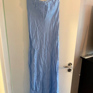 Ljusblå långklänning - Säljer en enkel och stilren ljusblå långklänning med rak passform. Klänningen är ärmlös och har en mjuk, flowy känsla som passar perfekt till sommarens tillfällen. Perfekt för dig som gillar minimalistisk stil.