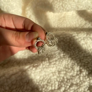 Glittriga örhängen med stenar - Säljer ett par glittriga örhängen i silverfärg med runda former och täckta av små gnistrande stenar. Perfekta för att ge en extra touch till din look. Snygga och trendiga accessoarer!