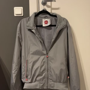 Grå vindjacka från Colmar - Säljer en stilren grå och unik vindjacka från Colmar Originals. Jackan har dragkedja framtill, ribbade muddar och två fickor med dragkedja. Klassisk och enkel design med Colmar-logga på insidan. Perfekt för vår. Storlek S/M. Skick 8/10 med tanke på den lila defekten under armen. Pris går att ändra vid snabb affär och tveka inte att höra av er vid minsta lilla fundering 