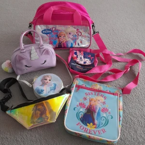 Flera färgglada barnväskor med Frost och enhörning - Säljer ett gäng söta väskor för barn, bland annat rosa handväska med Frost-motiv, liten lila enhörningsväska, holografisk magväska och axelväska med Anna & Elsa. Perfekt för att bära småsaker och accessoarer.