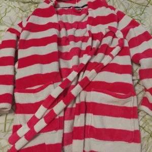 Rosa och vit randig morgonrock med bälte - Mysig morgonrock i rosa och vit randig design med lång ärm och matchande bälte i midjan. Två stora fickor framtill och mjukt material som känns skönt mot huden. Perfekt för att chilla hemma.