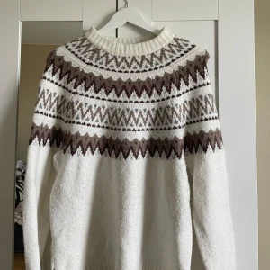 Vit och brun stickad tröja - Mysig stickad tröja från 157 i vitt med brunt mönster runt bröst och axlar. Tröjan har rund halsringning och långa ärmar. Perfekt för kyliga dagar och enkel att matcha med jeans eller kjol. Jul vibes🥰❤️