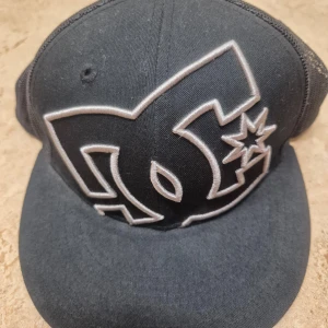 Svart keps från DC Shoes med mesh - Svart keps från DC Shoes med stort broderat logotyp framtill. Kepsen har mesh på baksidan och justerbar snapback för perfekt passform. Använt, men fortfarande fint skick.
