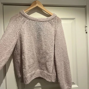 Stickad tröja med rosett - Superfin ljusrosa/beige stickad tröja med lång ärm och en svart rosett i nacken. Tröjan har en lite lös passform och ribbade muddar vid ärmslut och nederkant. Perfekt för mysiga dagar!