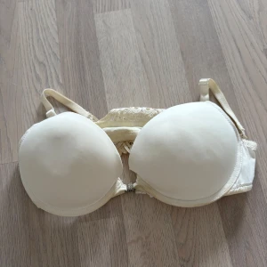 Vit spets-bh med strassdetalj Pusch up  - Säljer en vit bh med vadderade kupor och vacker spets i ryggen. Framtill finns en glittrig strassdetalj mellan kuporna. Axelbanden är justerbara och bh:n har fina spetsdetaljer både fram och bak. Missfärgad men går kanske bort strl 80C